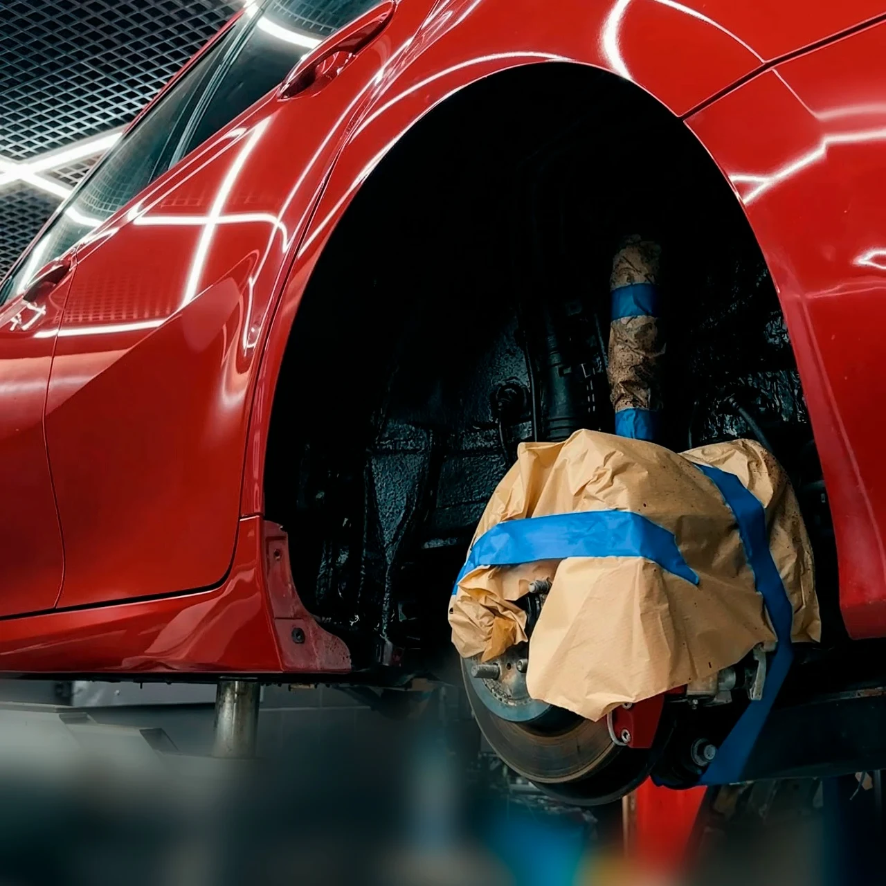 Красная Toyota Camry на подъёмнике во время защитной обработки арок и днища